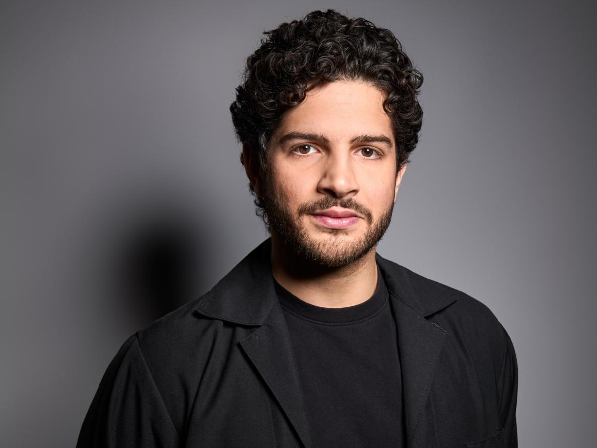 Das Bild zeigt den Schauspieler Payam Yazdani mit schwarzem Tshirt und schwarzem Hemd.