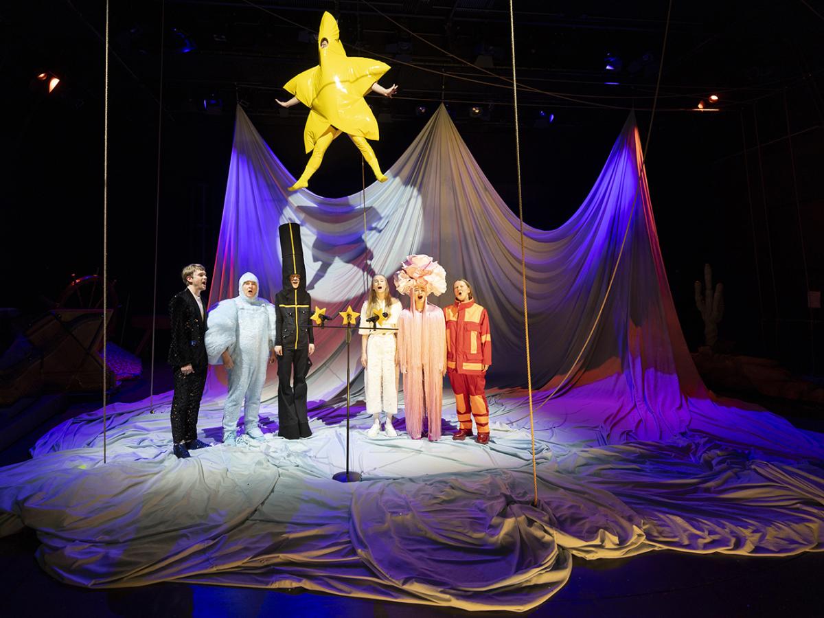 Das Foto zeigt sieben Schauspieler*innen in einer Stofflandschaft: Nico-Alexander Wilhelm, Hermann Book, Alicja Rosinski, Severin Mauchle (der als Stern verkleidet von der Decke schwebt), Lisa Wilhelm, Jara Bihler und Christine Ochsenhofer