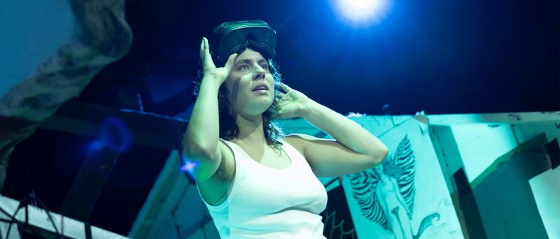 Anastasia Lara Heller trägt ein weißes Tank-Top und hat eine VR-Brille auf dem Kopf. Ihre Arme sind angewinkelt, die Finger berühren ihr Gesicht. Sie sieht in die Ferne, ihr Mund ist geöffnet. 