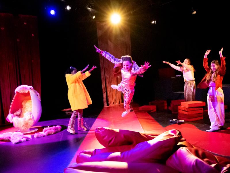 Das Bild zeigt 4 jugendliche Spieler*innen, die sich tanzend und springend über die Bühne bewegen.