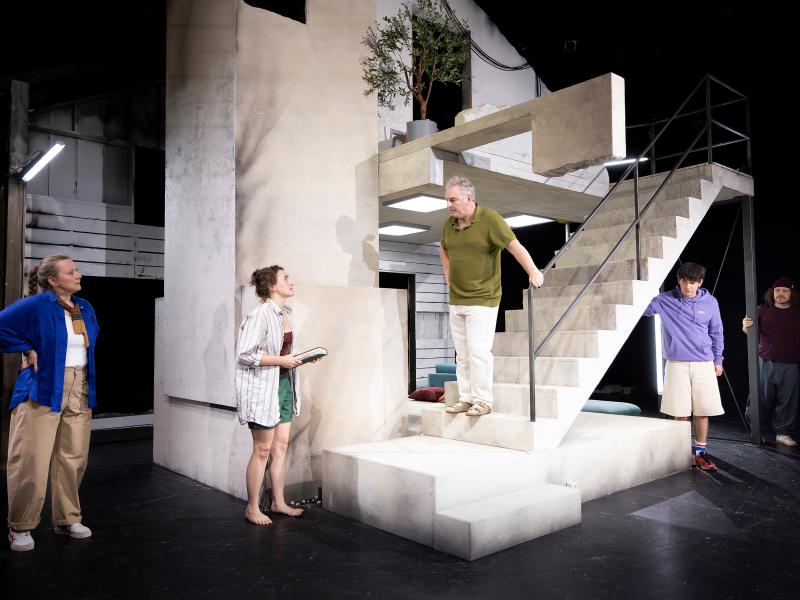 Das Ensemble steht verteilt im Bühnenbild. Hermann Book steht erhöht auf einer steinernen Treppe. Er und Victoria Kraft sehen sich an. Die anderen blicken in ihre Richtung.