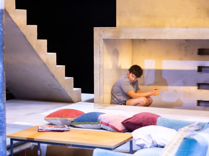 Silvio Kretschmer hockt in einer Steinnische. Im Vordergrund Kissen, ein Couchtisch und eine steinerne Treppe im Hintergrund.