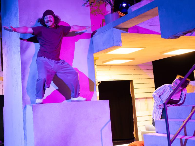 Parsa Yaghoubi Pour steht auf einem Steinvorsprung mit ausgebreiteten Armen und Beinen. Viktoria Kraft lehnt sich über die Steintreppe, um ihn sehen zu können. Beide lachen.