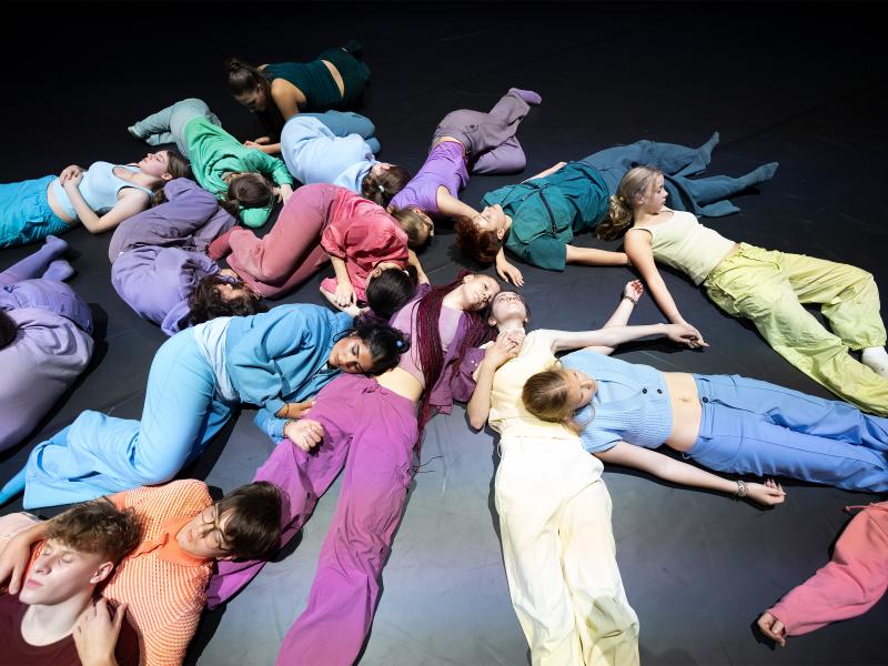 Die Tänzer*innen liegen durcheinander teils ausgestreckt, teils eingerollt auf dem Boden. Alle berühren sich dabei mal mehr, mal weniger.