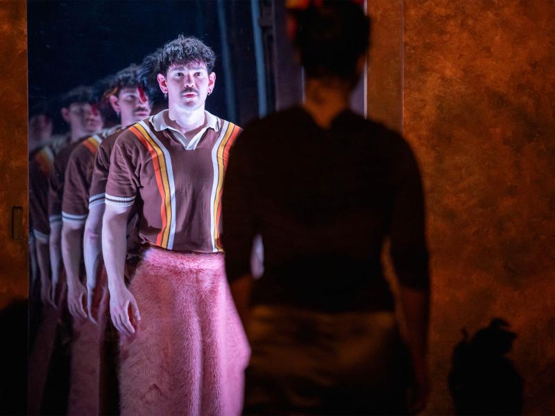 Bühnensituation: Silvio Kretschmer steht in braun-rosa Kleidung vor einem Spiegel, in dem er sich viele weitere Male spiegelt. Im Vordergrund steht mit dem Rücken zum Publikum eine weitere Person, die Silvio anschaut.