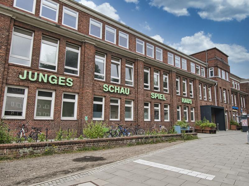 Das Bild zeigt das Gebäude des Jungen Schauspielhauses in Barmbek. Es ist ein roter, länglicher Klinkerbau. In hellgrünen Buchstaben steht Junges Schauspielhaus an der Fassade.